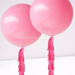 May include: Two large pink balloons with pink tassel tails. The balloons are inflated and tied together.
