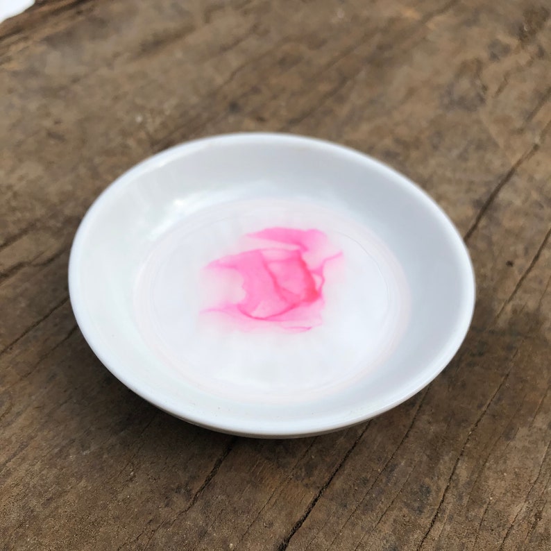 White ceramic jewelry dish with a pink metallic alcohol ink design