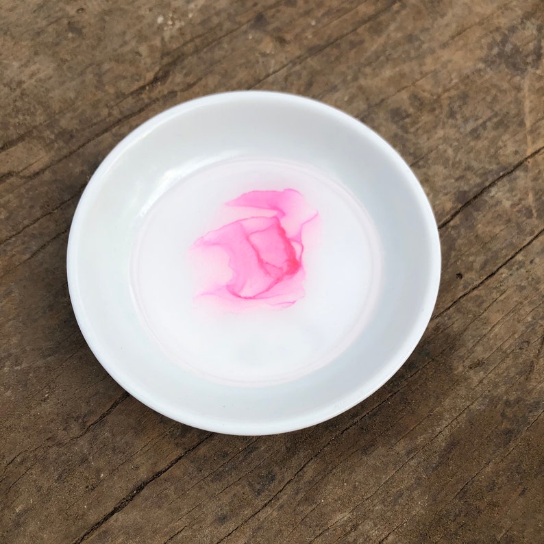 White ceramic jewelry dish with a pink metallic alcohol ink design