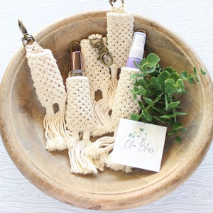 May include: Five crocheted keychains with tassels, each holding a small bottle of liquid. The keychains are in a wooden bowl with a small card that says "Ola Bliss".