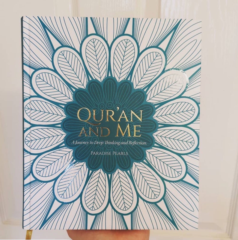 May include: A book titled "Qur'an and Me" with a teal and white floral design. The title is in gold lettering, with the subtitle "A Journey to Deep Thinking and Reflection." The book is held by a person.