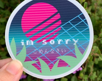 May include: A round sticker with a pink and blue sunset design. The sticker has the text "i'm sorry" in pixelated letters and the Japanese text "ごめんなさい" (gomen nasai) below it.
