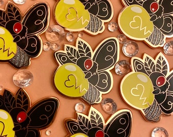 May include: Six black and gold enamel pins featuring a moth with a lightbulb. The moth has a red eye and the lightbulb has a yellow heart and a lightning bolt.