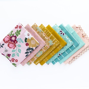 May include: A collection of folded fabric squares in various floral and geometric patterns. The color palette includes pink, burgundy, gold, and teal, creating a visually appealing arrangement. The fabrics are likely for quilting or crafting projects.