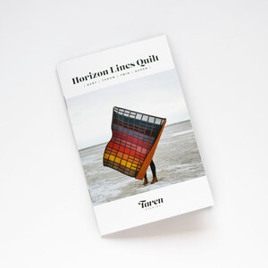 May include: A colourful quilt pattern with a geometric design. The quilt is folded in half and held by a person standing on a beach. The quilt is called "Horizon Lines Quilt" and is available in baby, throw, twin, and queen sizes. The text "Taren Studios" is at the bottom of the page.