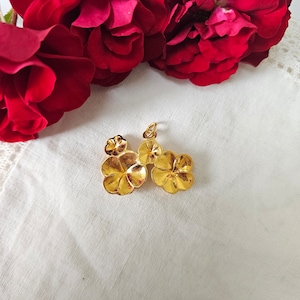 May include: A gold-colored pendant featuring a floral design with three flower clusters. The pendant is set against a white fabric background, with red roses in the upper portion of the image.