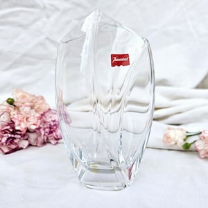 Può includere: Un vaso di vetro trasparente con un design moderno e unico. Il vaso ha un'etichetta che recita "Baccarat".