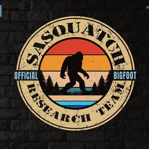 May include: A vintage-style round badge with the text "Sasquatch Official Research Team Bigfoot" in a circle. The badge has a retro sunset design with a silhouette of Bigfoot walking through a forest.