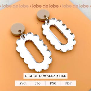 May include: A pair of silver earrings with a scalloped edge and a mirror-like finish. The earrings are hanging from beige, round, clay-like posts.