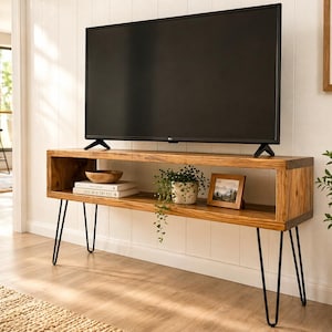 May include: A wooden TV stand with a rectangular design and black hairpin legs. The stand has an open shelf with a bowl, books, a framed photo, and a potted plant. A large black television sits on top.