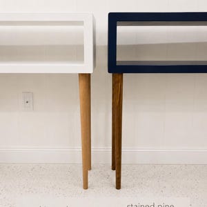 May include: Two modern console tables, one white oak and one stained pine special walnut, are displayed side-by-side. Each table has a rectangular top and tapered legs. The white table is on the left, and the walnut table is on the right.