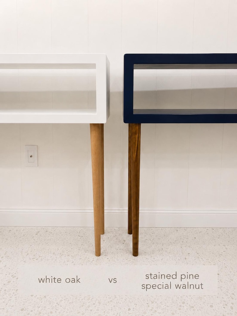 May include: Two modern console tables, one white oak and one stained pine special walnut, are displayed side-by-side. Each table has a rectangular top and tapered legs. The white table is on the left, and the walnut table is on the right.