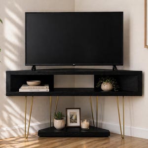 Puede incluir: Mueble de TV esquinero negro con un televisor de pantalla plana. El mueble tiene patas doradas de horquilla y un estante inferior con objetos decorativos, incluyendo una peque&ntilde;a planta, una foto enmarcada y una vela. El mueble es de madera.