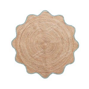May include: A round jute rug with a scalloped edge. The rug is a natural tan color with a light blue border. The rug has a woven texture and is suitable for indoor use.