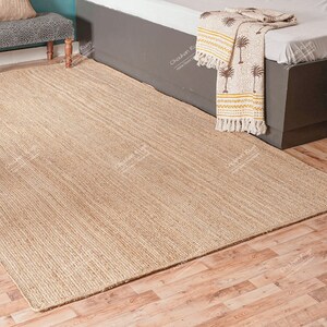 May include: A natural fiber rug with a woven texture in a light beige color. The rug is laid out on a wooden floor.