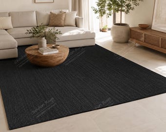 May include: A large, rectangular area rug featuring a solid, deep black color and a textured, woven surface. The rug is positioned flat on a light-colored floor, extending from the foreground toward the center of the room under a wooden coffee table.