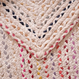 May include: A close-up of a woven rug with a chevron pattern. The rug is made of various colors of fabric, including white, pink, red, blue, and yellow.
