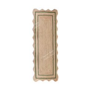 May include: A rectangular jute rug with a scalloped edge and a green border. The rug has a natural, woven texture and a neutral color palette, suitable for various interior styles. The rug's dimensions are not visible.