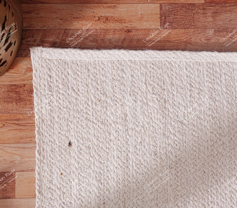 "A minimalist and highly textured hand-braided jute rug, presented in a clean, natural off-white/ivory tone. The vertical weave pattern creates subtle visual depth, while the overall simple design makes it a versatile foundation piece perfect for adding organic warmth and understated elegance to any modern or coastal living space."