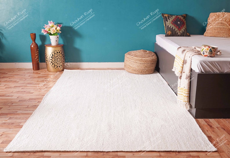 "Captured from above on a crisp white background, this durable rectangular area rug showcases the rustic beauty of undyed natural jute. The meticulous braided construction is visible through the slight variations in fiber and tone, emphasizing its authentic, artisan-made quality and soft, neutral aesthetic."