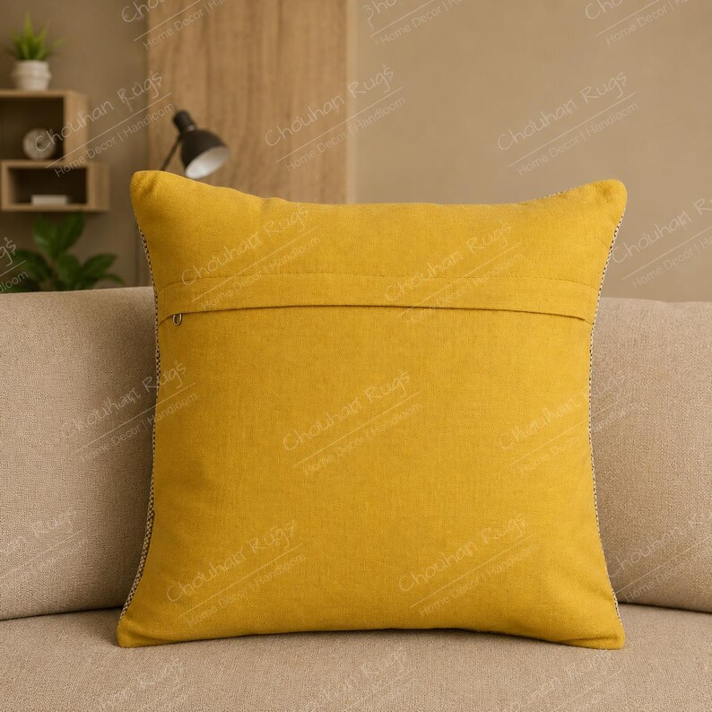 May include: A square mustard yellow throw pillow cover featuring a horizontal seam across the center and a visible zipper closure. The fabric has a textured appearance, and the edges are finished with a thin, dark, contrasting piped trim.