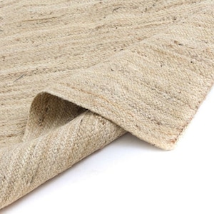 May include: A close-up of a natural fibre rug with a woven texture. The rug is folded in half, revealing the underside of the weave. The rug is a light beige colour.