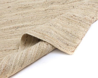 May include: A close-up of a natural fiber rug with a woven texture. The rug is folded in half, revealing the underside of the weave. The rug is a light beige color.