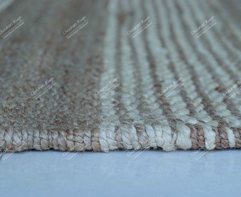 K&ouml;nnte beinhalten: Nahaufnahme eines Naturfaser-Teppichs mit einem gestreiften Muster. Der Teppich ist aus Jute und hat eine hellbraune und wei&szlig;e Farbgebung. Der Teppich ist mit einer dichten Webart gewebt und hat eine leicht strukturierte Oberfl&auml;che.