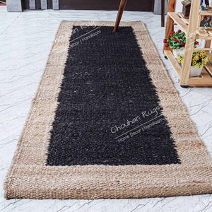 May include: A black and natural jute rug with a black border. The rug has the text "Chouhan Rugs Home Decor | Handloom" printed on it.