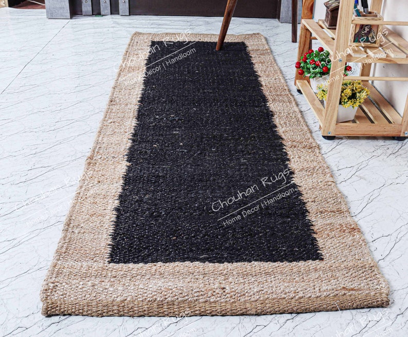 May include: A black and natural jute rug with a black border. The rug has the text "Chouhan Rugs Home Decor | Handloom" printed on it.