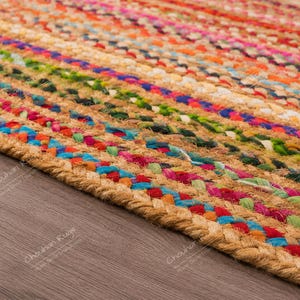 May include: A rectangular area rug constructed from braided natural jute fibers interwoven with vibrant multi-colored fabric strips. The design features repeating horizontal bands of red, blue, green, yellow, and pink, creating a textured surface.