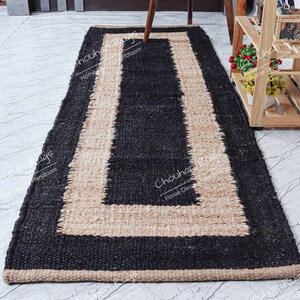 May include: A black and natural jute rug with a border. The rug has a rectangular shape and is made of natural fibers.