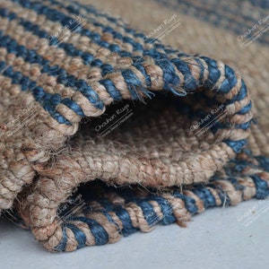 K&ouml;nnte beinhalten: Nahaufnahme eines gewebten Jute-Teppichs mit blauen Streifen. Der Teppich ist in der Mitte gefaltet und zeigt die Textur und die Details der Webart.
