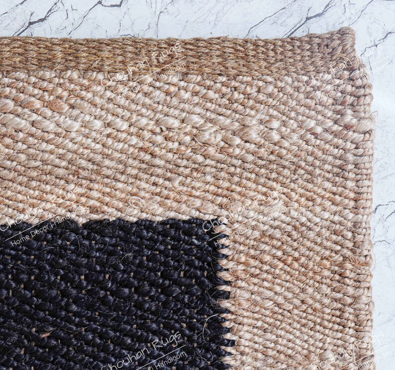 May include: Close-up of a woven jute rug with a black and beige geometric pattern. The rug has a natural, earthy feel and is perfect for adding a touch of texture to any room.