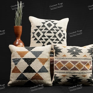 Op de afbeelding: Drie decoratieve kussens met geometrische patronen in zwart, wit, bruin en oranje. De kussens zijn gemaakt van geweven stof en hebben een handgeweven textuur.