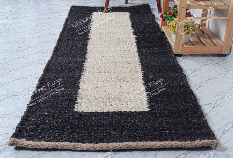 May include: A black and white jute rug with a rectangular white center and a black border. The rug has a fringe border.