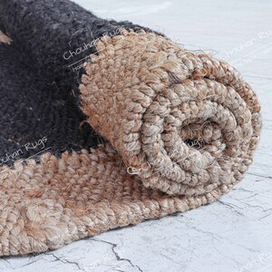 May include: Close-up of a rolled-up jute rug with black and natural brown stripes. The rug is made of natural fibers and has a rough texture. The text "Chouhan Rugs Home Decor Handloom" is visible on the rug.