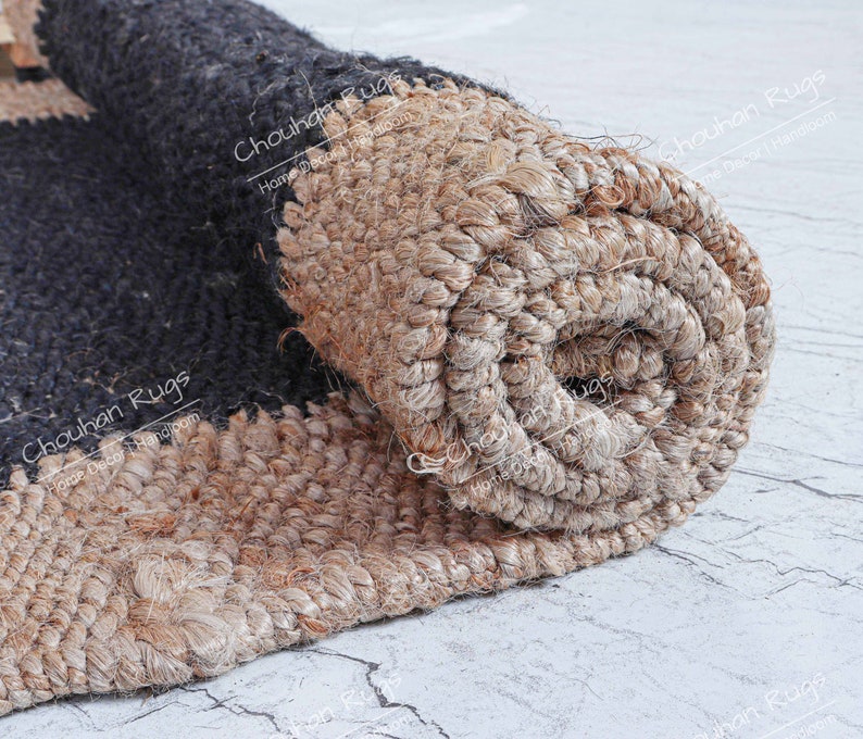 May include: Close-up of a rolled-up jute rug with black and natural brown stripes. The rug is made of natural fibers and has a rough texture. The text "Chouhan Rugs Home Decor Handloom" is visible on the rug.