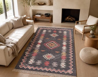 May include: A rectangular area rug featuring a dark gray base with a geometric pattern in shades of red, orange, white, and light gray. The rug has a zigzag border and fringe on the short ends, with the text "Chohan Rug" printed on the surface.
