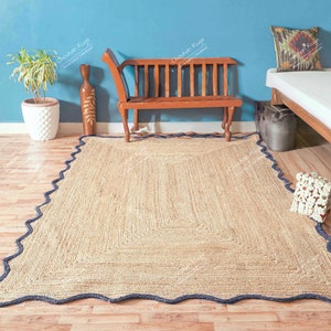 May include: A natural fibre rug with a blue border and a scalloped edge. The rug is laid out on a wooden floor in a room with a wooden bench and a white bed.