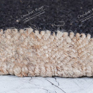 May include: Close-up of a jute rug with a black and natural color combination. The rug is handwoven and has a textured surface. The text "Chouhan Rugs Home Decor | Handloom" is visible in the image.