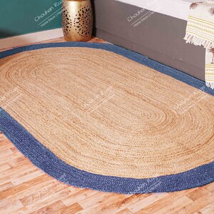 K&ouml;nnte beinhalten: Ovaler Jute-Teppich mit blauem Rand. Der Teppich ist aus Naturfasern gefertigt und hat einen rustikalen, erdigen Look.