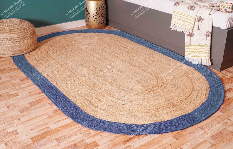 K&ouml;nnte beinhalten: Ovaler Jute-Teppich mit blauem Rand. Der Teppich ist aus Naturfasern gefertigt und hat einen rustikalen, erdigen Look.