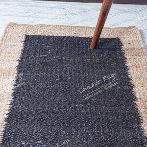 May include: A black and natural jute rug with a black center and a natural jute border. The rug has a rough, textured surface. The text "Chouchan Rugs" is printed in white on the black center of the rug.