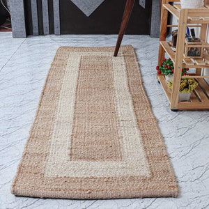 Op de afbeelding: Een vloerkleed van natuurlijke vezels met een witte rand. Het vloerkleed is gemaakt van jute en heeft een rechthoekige vorm.