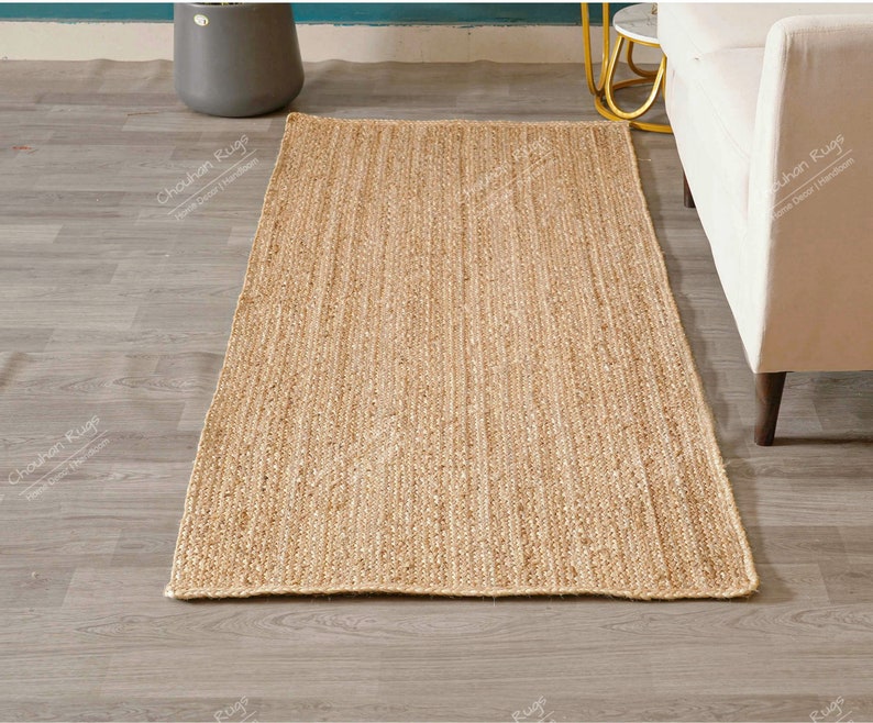 "Captured from a top-down view on a white background, this durable mat showcases the inherent beauty and linear texture of natural jute fiber. The consistent, dense braiding along the length ensures resilience and provides a soft, earthy aesthetic ideal for layering or high-traffic areas."