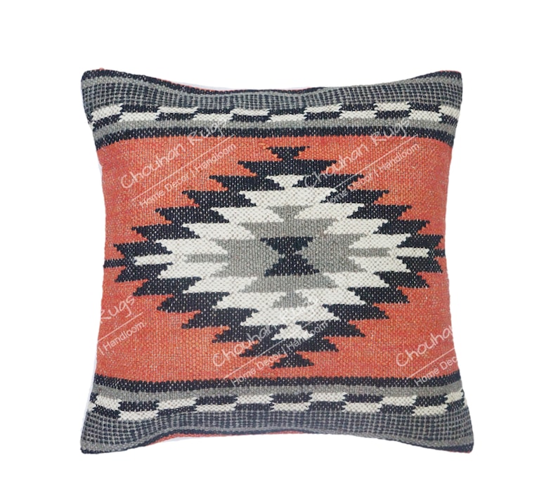 May include: A square throw pillow featuring a central geometric diamond pattern in shades of black, gray, and white against a textured burnt orange background. The top and bottom borders display a black and white checkered motif. Text reads Chouhan Rugs Home Decor Handloom.