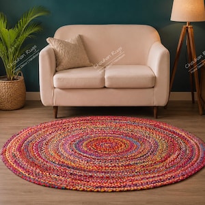 May include: A round, braided area rug featuring a vibrant, multi-colored pattern with concentric circles of red, pink, orange, yellow, blue, and purple fibers. The rug has a thick, textured weave and is positioned flat on a light wood floor.