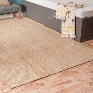 May include: A natural fibre rug with a woven texture in a light beige colour. The rug is laid out on a wooden floor.