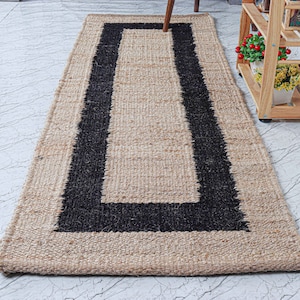 Op de afbeelding: Een vloerkleed van natuurlijke vezels met een zwarte rand. Het vloerkleed is gemaakt van jute en heeft een rechthoekige vorm.